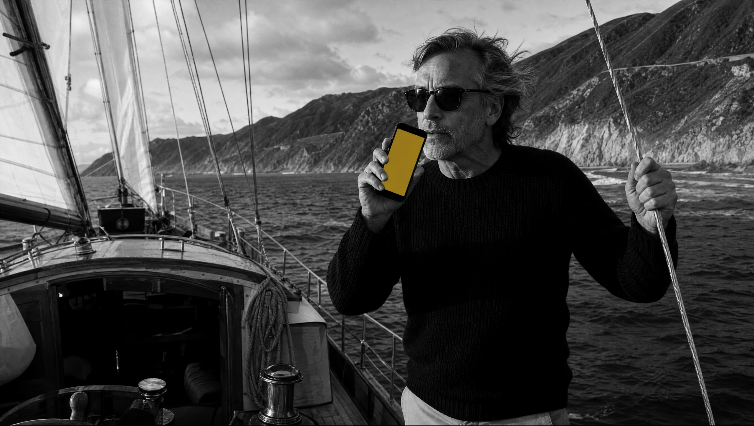 A man at the rail of a sailboat off the Big Sur coast, speaking into his phone